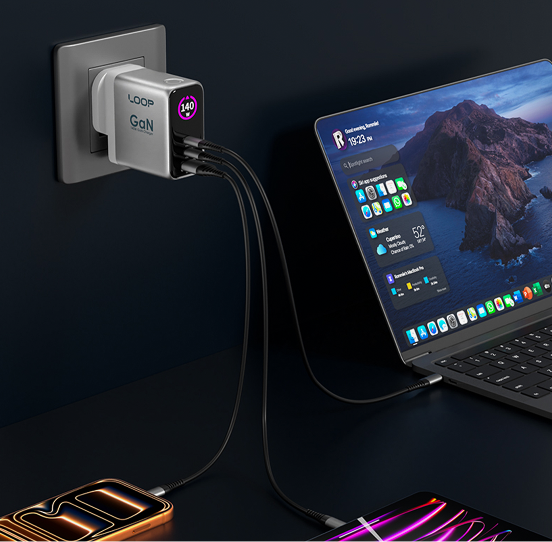A LOOP Goli portable charger plugged into a wall outlet, connected to a laptop and phone on a dark desk.